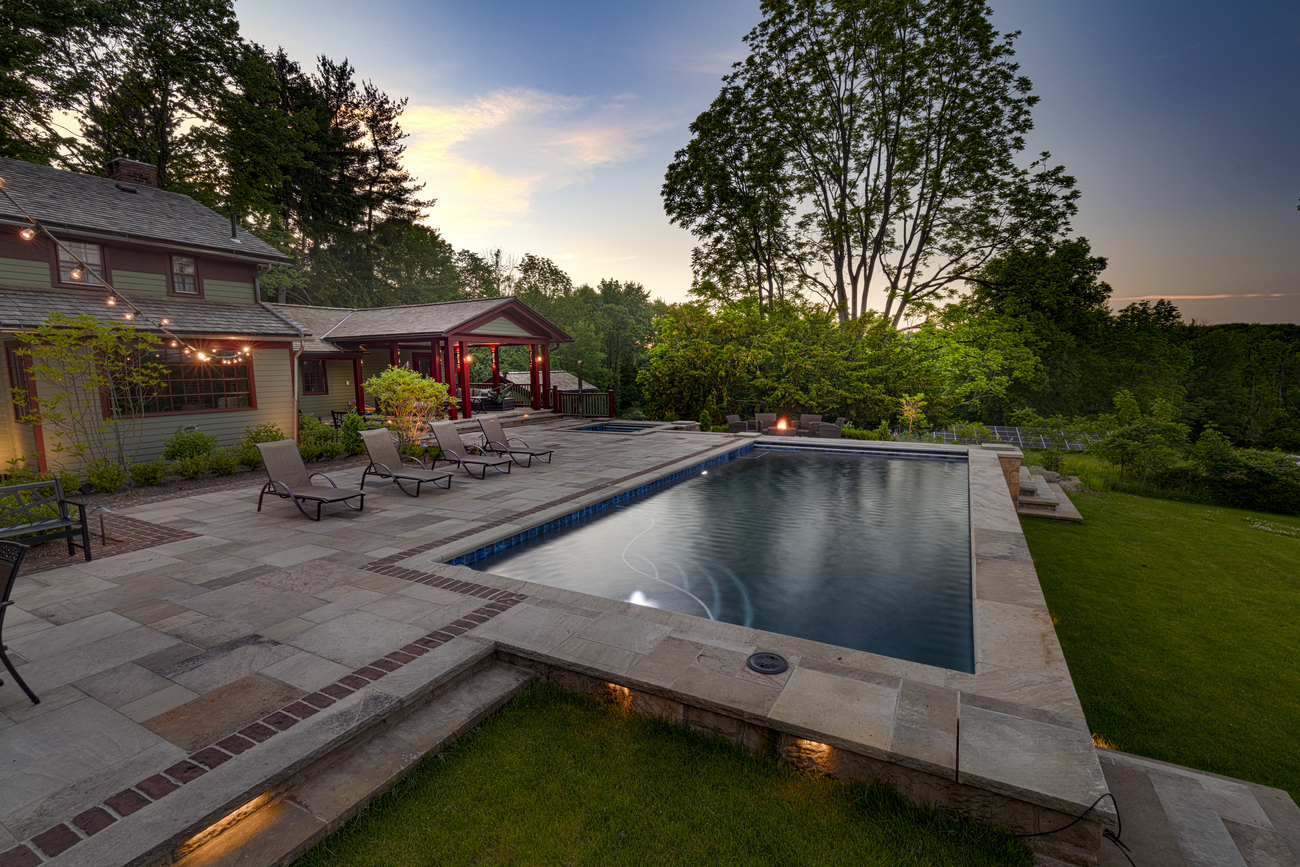 Rectangular swimming pool in front of a large field, pictured at dusk.