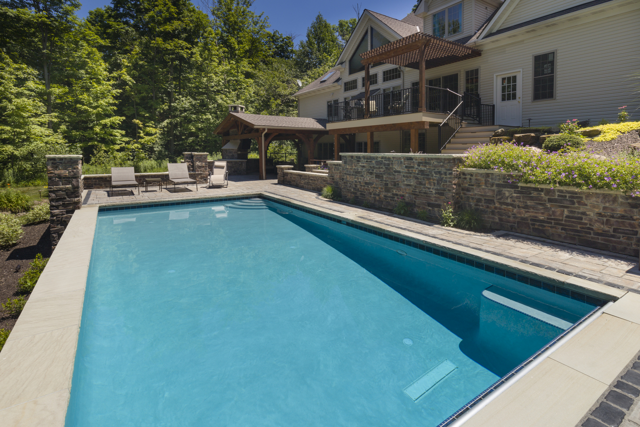 Rectangular residential pool installed in front of a large wooded area.