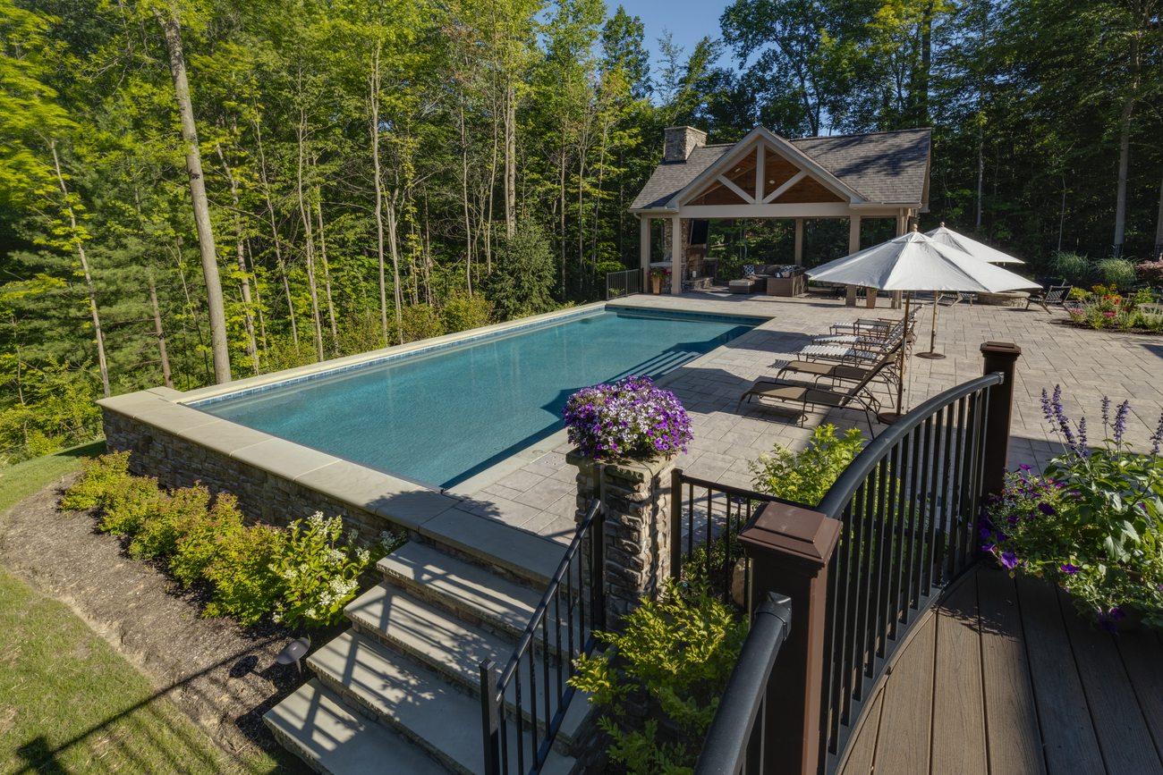 Rectangular residential pool in front of large wooded area.
