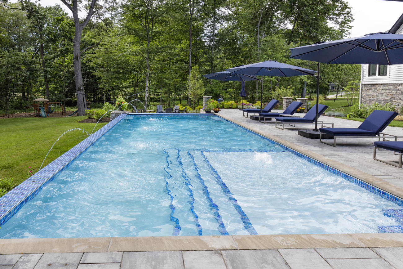 Rectangular residential swimming pool in front of navy deck chairs.