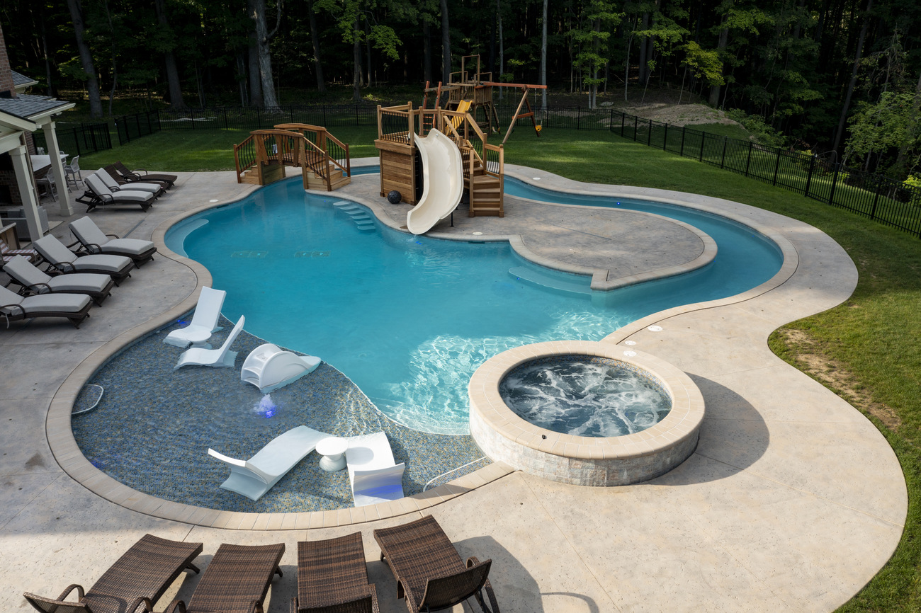 Freeform residential pool with wooden children's play area.