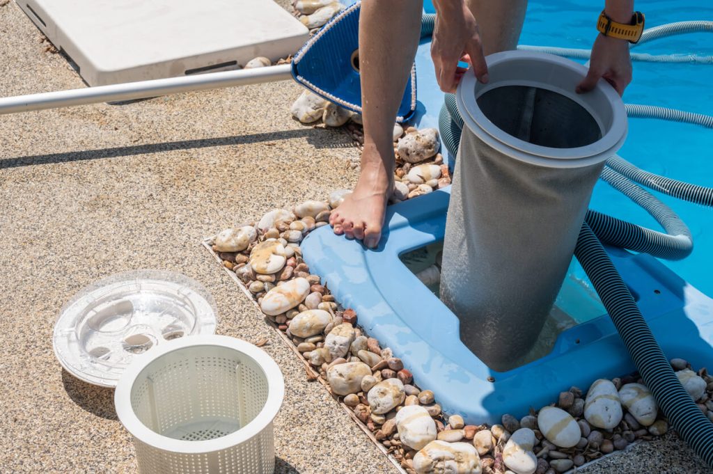 Person cleaning a pool filter cartridge beside swimming pool.